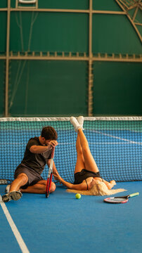 A young couple resting on a blue indoor tennis court after a long and intense practice session
