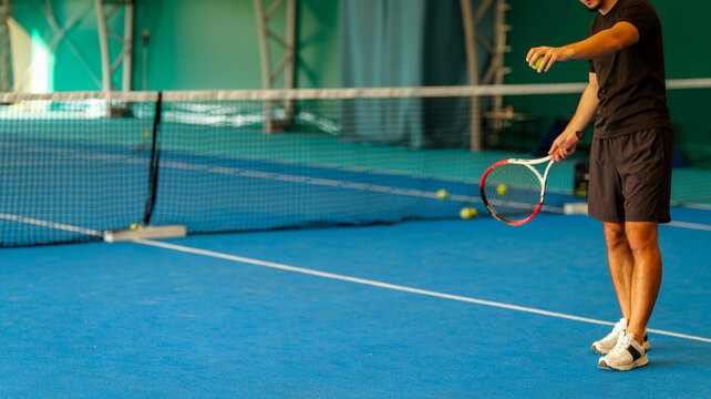 A tennis player preparing to serve on a vibrant blue indoor court with a racket and yellow ball