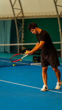 A focused young man preparing to serve a tennis ball on an indoor blue hard court surface area