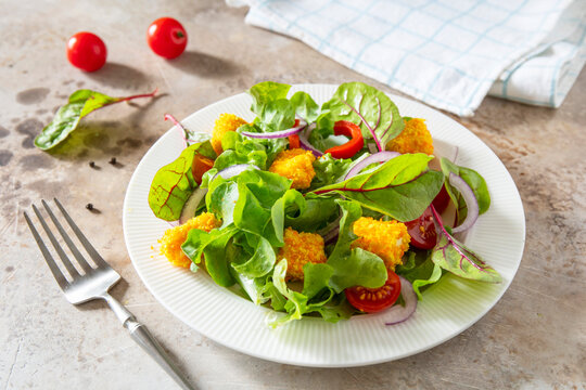 Summer fresh vegetable salad with crispy breaded feta cheese on a textured stonesurface. Tasty appetizer ready to eat.
