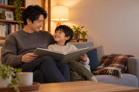 読書の秋に絵本を楽しむ日本人の父親と息子、温かなリビングで会話と笑顔が生まれる親子の読み聞かせ時間-生成