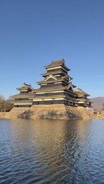 Black Matsumoto Castle reflected in the moat under a clear blue sky