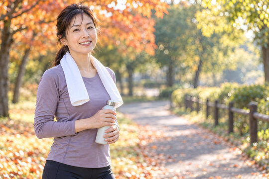 紅葉の公園で朝のランニングを終えた日本人の40代女性、爽やかな笑顔と達成感が伝わる秋の運動習慣-生成
