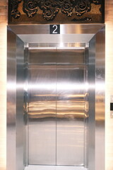 Sleek metallic elevator doors with a reflective polished surface, displaying the number two above, illustrating modern interior architecture and vertical transportation in a contemporary building © Satriyo