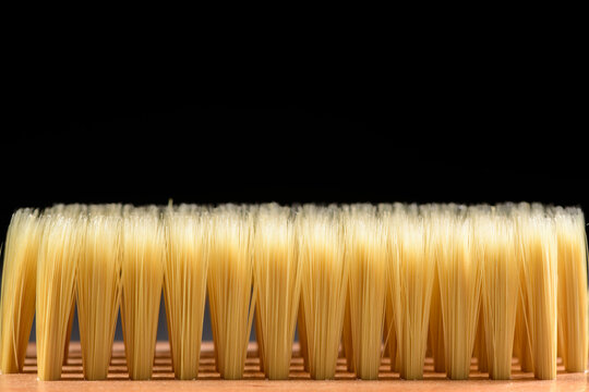 Close-up detail of natural bristle paintbrush with uniform golden-yellow fibers aligned in rows against dark background, professional painting tool and construction equipment
