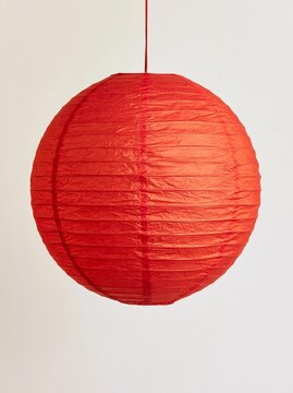 The image is of a round, red paper lantern hanging from a red string. the lantern appears to be made of paper and has a textured surface with vertical lines running horizontally across it.