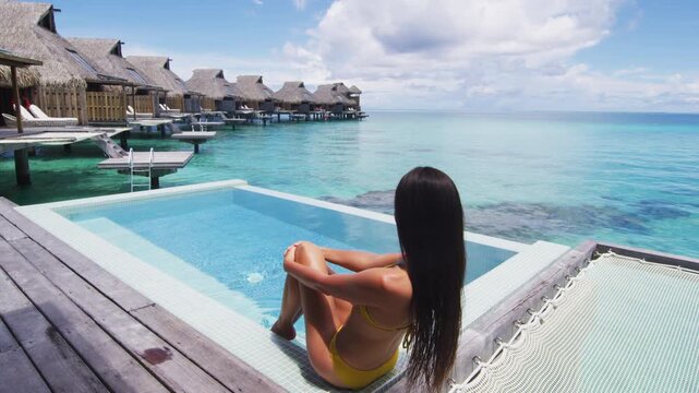 Luxury travel vacation resort destination at idyllic overwater bungalow villa. Woman relaxing by infinity pool. Raw unedited video of real unretouched woman model without any makeup