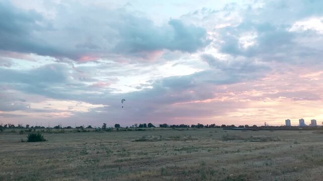 Paraglider soaring over open dry field during colorful sunset with pink and blue cloudy sky