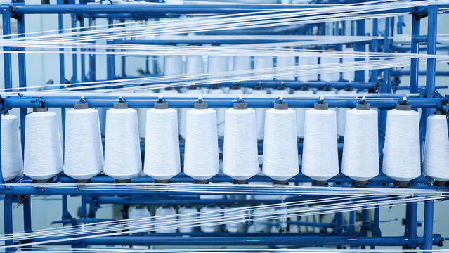 Industrial textile machinery holding multiple white yarn spools arranged on blue metal racks for production.
