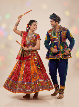 Indian folk dance couple performing dandiya together in colorful embroidered traditional costumes