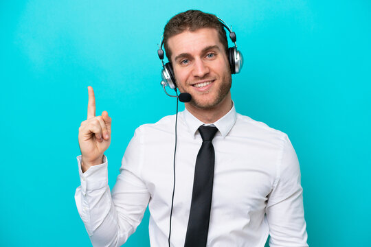 Telemarketer caucasian man working with a headset isolated on blue background showing and lifting a finger in sign of the best