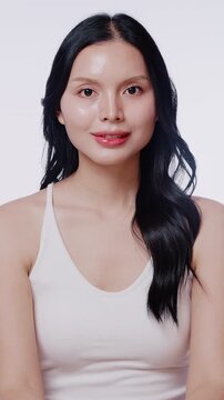 A beautiful Asian woman with clean glowing skin smiles at the camera. Perfect for skincare, beauty product, and cosmetic advertisements.