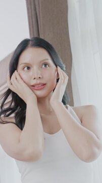 Beautiful Asian woman touching her smooth cheeks with a smile. She shows healthy and glowing clear skin.