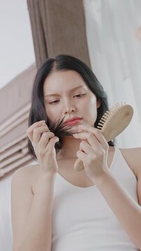 An Asian woman inspects split ends and damaged hair with a worried look. Perfect for hair problem, repair treatment, and hair health commercials.
