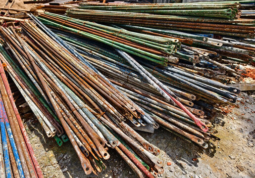 Rusted steel rebar rods stacked outdoors at construction site with dusty ground
