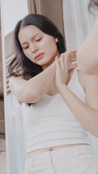 A concerned Asian woman examining dry skin on her arm in front of a mirror.
