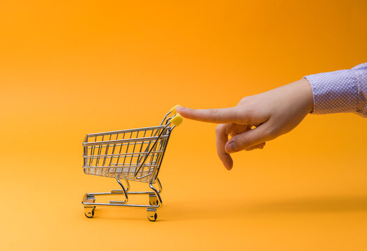 Hand Pushing Small Shopping Cart on Orange Background for Budget Savings