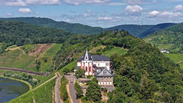 Spektakul&auml;re Drohnenaufnahme der historischen Marienburg auf dem schmalen Bergr&uuml;cken der Moselschleife bei Zell, umgeben von sonnigen Weinh&auml;ngen.