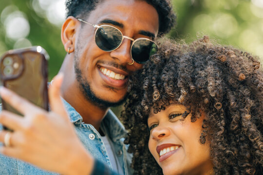 happy young couple smiling and taking a selfie together outside. They look joyful and relaxed in a green park setting