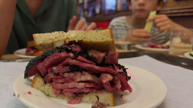 Close-up view of a towering pastrami sandwich on rye bread with mustard, a classic american dish served on a white plate in a traditional new york delicatessen diner