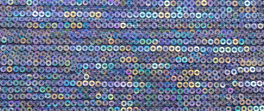 Holographic sequin texture with rows of shiny circular spangles. Close up of iridescent glitter fabric background