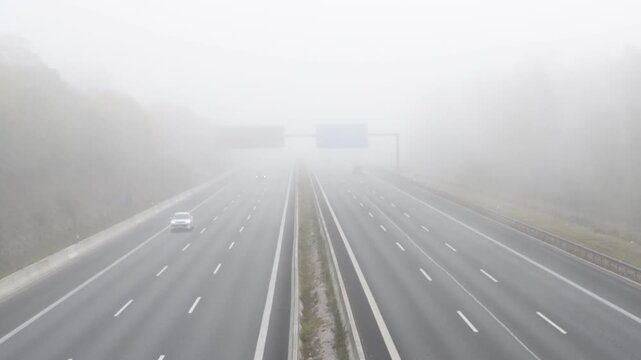 Cars driving on a highway during a dense morning fog with low visibility and road traffic