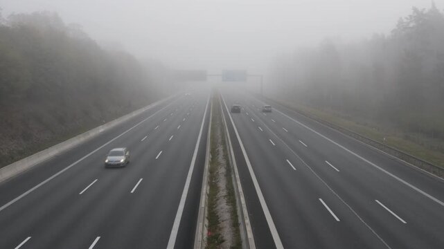 Cars driving on a multi-lane highway during a dense morning fog with low visibility conditions