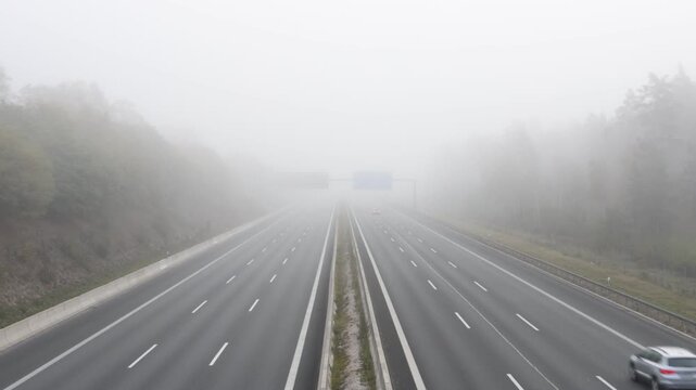 Cars driving on a multi-lane highway through dense morning fog in the countryside landscape