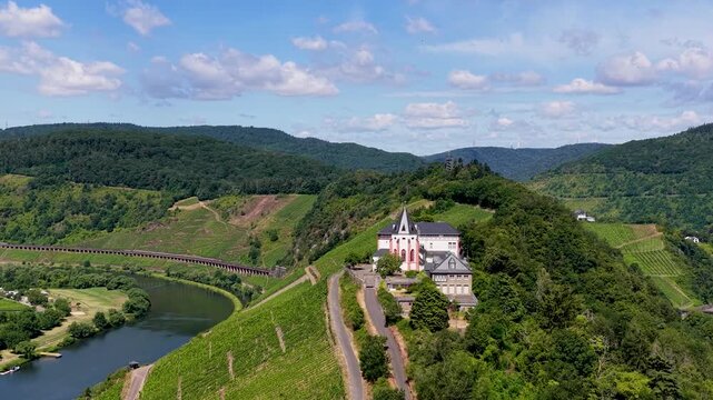 Spektakul&auml;re Drohnenaufnahme der historischen Marienburg auf dem schmalen Bergr&uuml;cken der Moselschleife bei Zell, umgeben von sonnigen Weinh&auml;ngen.