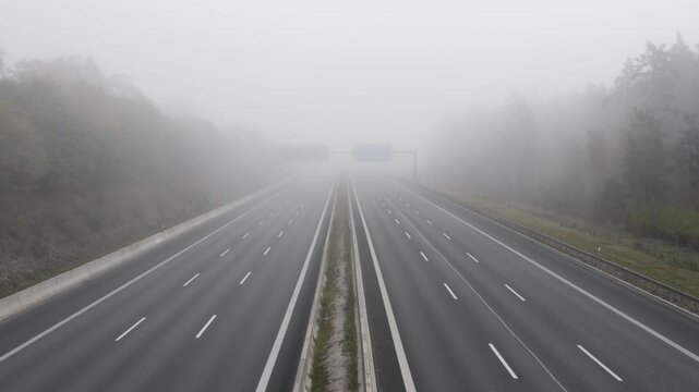 Cars driving on a multi-lane highway through dense morning fog in the countryside landscape