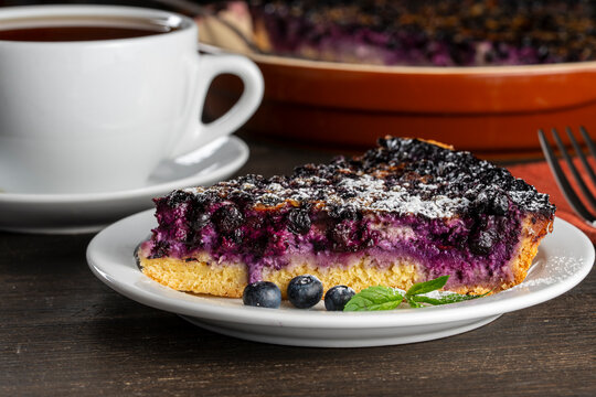Slice of homemade blueberry pie on plate with tea cup. Close up of delicious blueberry cake piece on white plate. Sweet berry tart dessert with fresh blueberries and mint for bakery or cafe menu