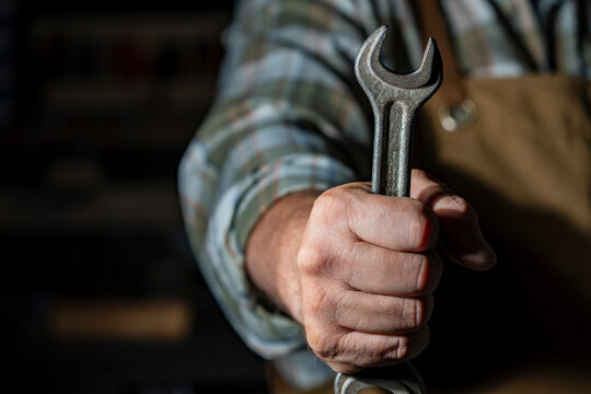 Mechanic hand holding metal wrench tool in workshop. Closeup of worker hand holding spanner tool. Plumber, repairman or mechanic expert in uniform ready for service and maintenance concept