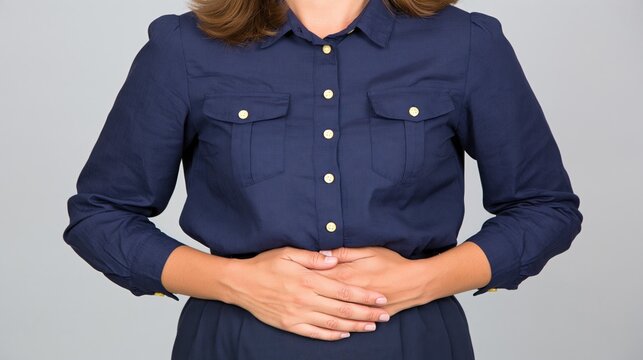 A woman holding her stomach in pain from discomfort. A person in dark blue t-shirt dress experiencing bloating. Hands on a belly due to digestive disorder