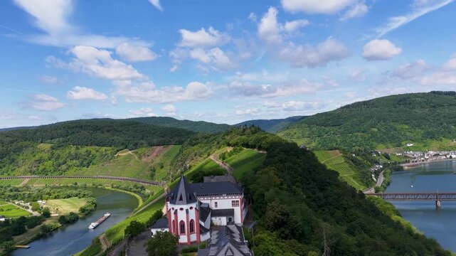 Spektakul&auml;re Drohnenaufnahme der historischen Marienburg auf dem schmalen Bergr&uuml;cken der Moselschleife bei Zell, umgeben von sonnigen Weinh&auml;ngen.