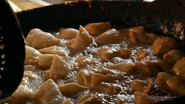 Samosas deep frying in a large iron wok. Golden, crispy samosas deep-frying to perfection in hot bubbling oil inside a traditional iron wok. It is a fried pastry filled with a spiced and potato.