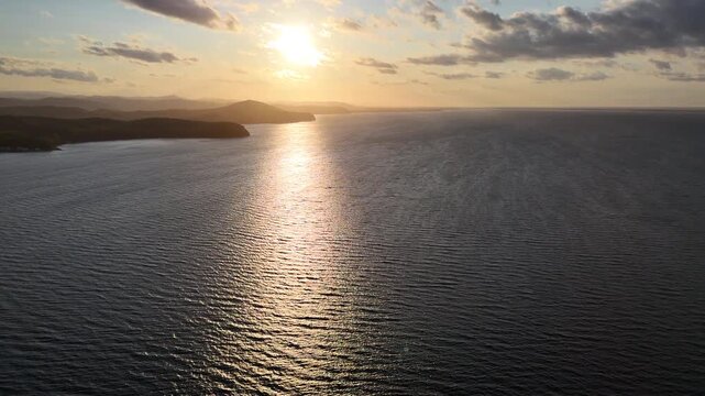 Low sun casting golden reflections across water and a distant coastline, aerial panorama