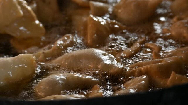 Samosas deep frying in a large iron wok. Golden, crispy samosas deep-frying to perfection in hot bubbling oil inside a traditional iron wok. It is a fried pastry filled with a spiced and potato.