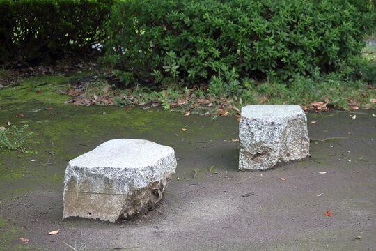公園の苔むした地面に置かれた御影石のシンプルな腰掛け石とベンチ