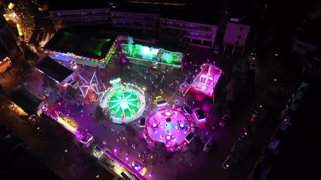 Aerial perspective of the annual Oldenzaal Najaarskermis (autumn fair) at night. Drone footage showing colorful illuminated funfair rides, neon lights, glowing carnival attractions, and the atmospheri