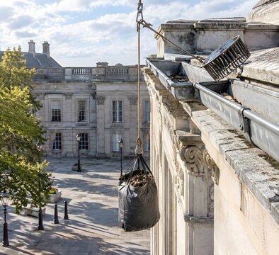 Aluminium gutter run on a stone civic building parapet with outlet strainer lifted out and rope hoist