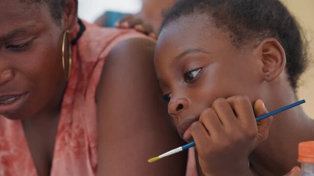 Child and parent participate in family art or group drawing painting workshop. scene shows close up interaction with visible materials like brushes for kids creative expression emphasizing