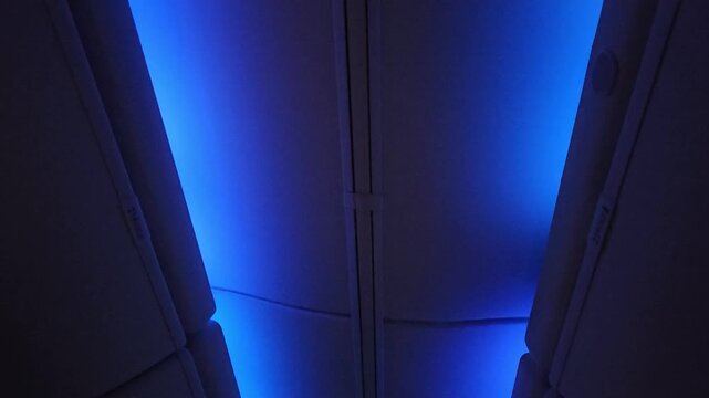 Blue ambient LED lighting illuminates the aircraft cabin ceiling and overhead bins, conveying a calm, modern atmosphere during a night flight. Ideal for travel, aviation, and transportation concepts.