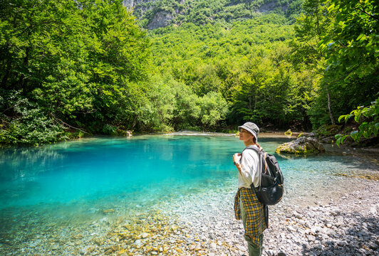 Female hiker standing on shore of Oko Skakavice spring and looking at majestic mountain landscape in Prokletije, Montenegro.