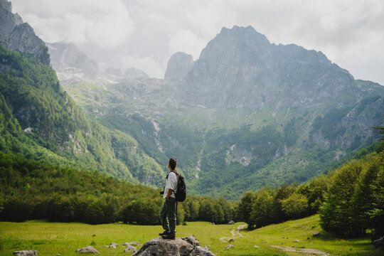 Woman hiker with backpack standing on a rock looking at Prokletije mountains in Montenegro.