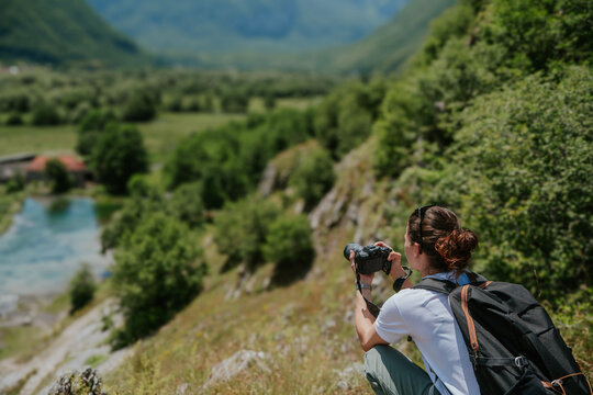 Woman photographer with camera squatting on a mountain top and looking at a scenic view.