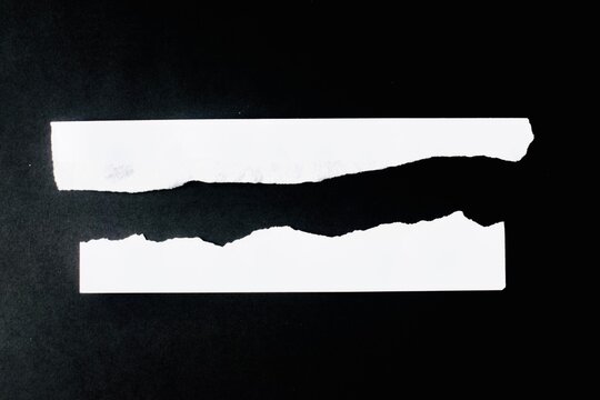 Two horizontal torn white paper strips placed parallel on a solid black background flat lay top view.