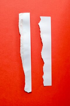Two vertical torn white paper strips with rough edges isolated on a bright red background flat lay top view.