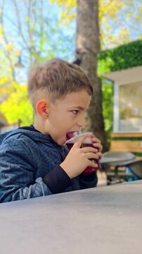 Little boy drinks bubble tea at an outdoor cafe in an autumn park, enjoying a sweet drink surrounded by trees, warm seasonal colors and a relaxed atmosphere during a beautiful fall afternoon