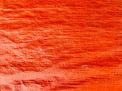 Texture detail of a bright orange woven polypropylene plastic tarp surface showing crisscross fiber pattern.
