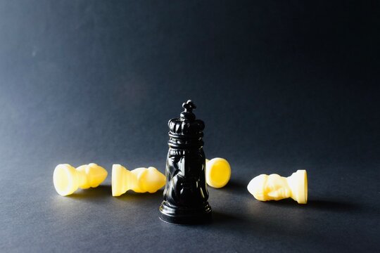 Black king chess piece standing amidst fallen white pawns scattered horizontally across a dark surface.